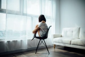 woman sitting on black chair in front of glass-panel window with white curtains seasonal depression