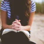 woman sitting on brown bench while reading book