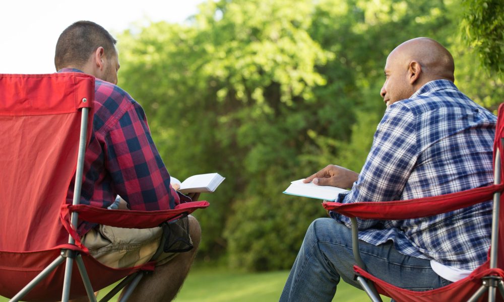 Multi-Ethnic group of friends talking and having a bible study. Men having a bible study on a camping trip.