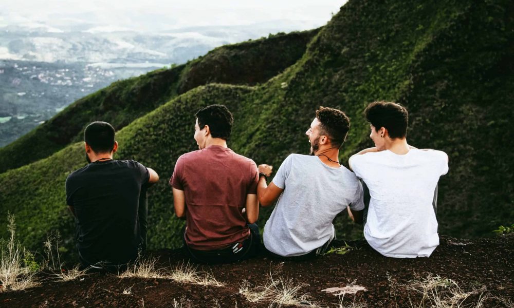 Photo by Matheus Ferrero row of four men sitting on mountain trail
